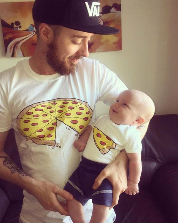 Man with a picture of a pizza pie on his T-shirt that is missing 1 slice, along with baby with pic of one slice.