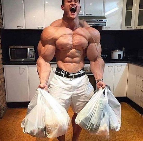 Muscular dude taking out the garbage in a nice kitchen.