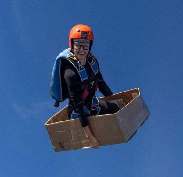 cool picture of girl in full skydiving outfit sitting in a box as she falls through the sky.