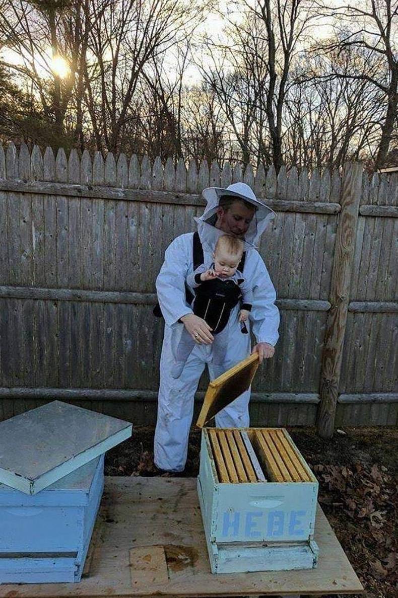 Man tending the bees while holding unprotected toddler in front of his bee suit.