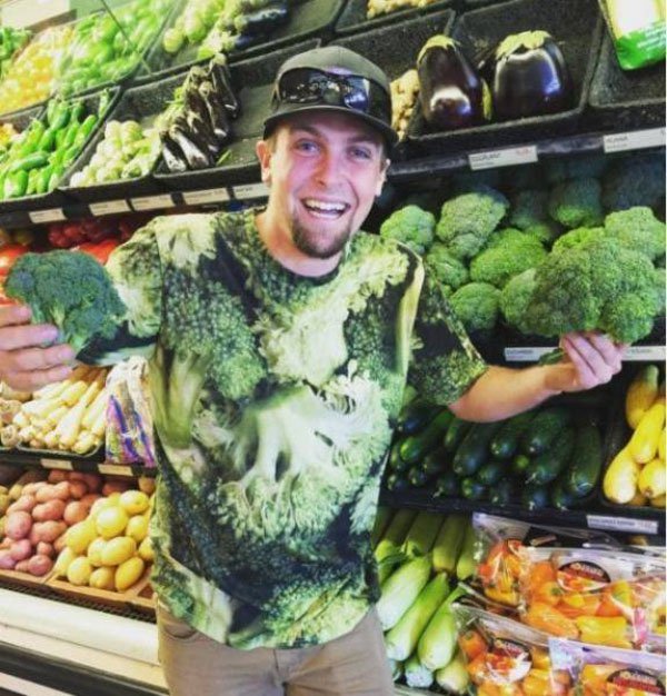 Man with broccoli shirt in the produce section of a supermarket.
