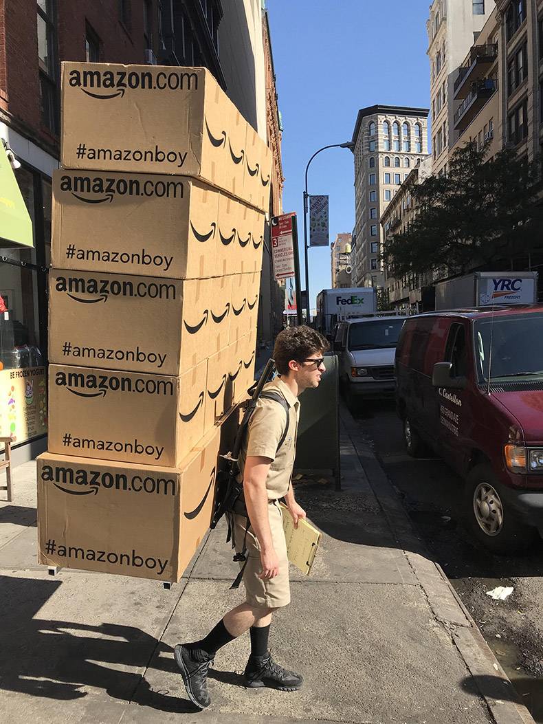 Man carrying large amount of Amazon boxes on his back.