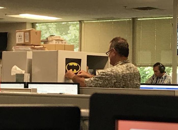man in the office putting up the Batman insignia upside down