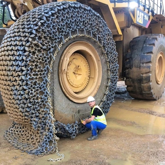 Cool pic of man putting massive chains on enormous tire of humongous dump truck