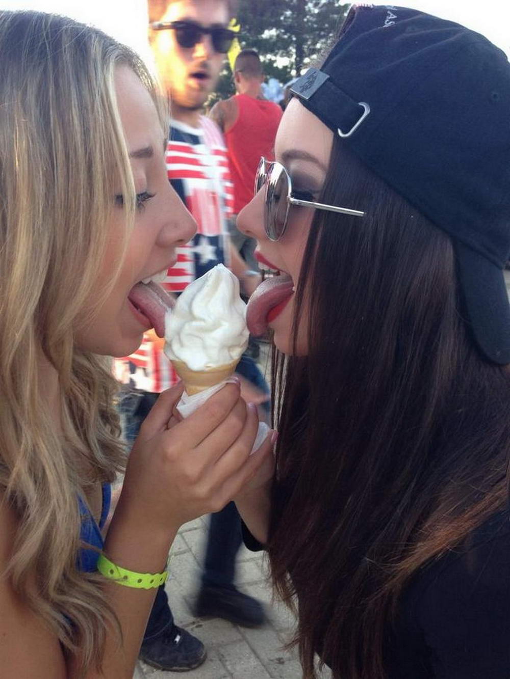 two girls lick ice cream cone while guy watches in the background