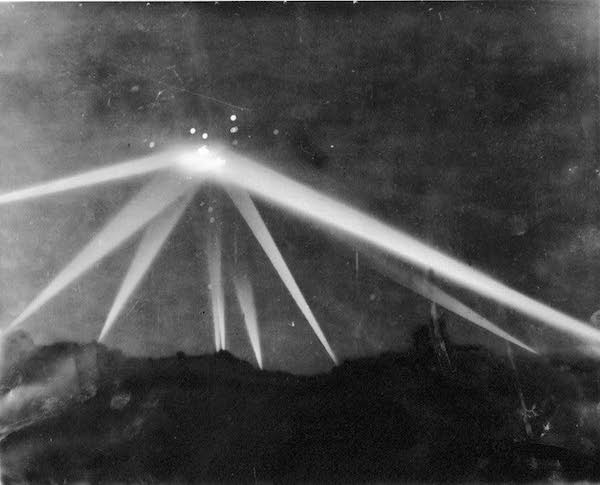 The Battle of Los Angeles is still thought by many to be one of the few "unexplained" UFO phenomena.

LA was consumed by "invasion jitters" at the time. A mere 79 days before the "battle," the Japanese had attacked Pearl Harbor, and the country was still reeling from the tragedy. There was widespread speculation that the West Coast was going to be next. 

On February 24-25, 1942, air raid sirens sounded throughout Los Angeles County. At 3:16 am the anti-aircraft batteries went crazy, lobbing shells and firing machine guns at reported aircraft from Santa Monica to Culver City. Over 1,400 rounds were fired during the alert and the vigorous shelling was witnessed by thousands on the ground. Eight people died as a consequence of this anti-aircraft fire—five from falling shrapnel and three from heart attacks. 

But what, if anything, triggered the event? Would you believe—weather balloons? 

In 1983, the Office of Air Force History concluded that balloons were indeed responsible for inciting mass hysteria. They were released from each of the dozen anti-aircraft positions around the city every six hours and were illuminated from below by an enclosed candle that would reflect off the silver lining of the balloon itself to ensure that it was visible at night. A U.S. Army memo to President Roosevelt suggests that gunners from all but one battery mistook the balloons for planes and opened fire. The memo also stated there was no evidence of bombs being dropped, troop casualties reported, or planes shot down. The President's response was to suggest that the power to order an air alarm should be restricted to U.S. Army officials only. 

And as for the above photo—it was heavily doctored. Before and after comparisons show that separate round spots of light seen where the beams converge (most likely lens flares) were modified with blobs of white paint, inadvertently creating an impression of an object "trapped" in the beams.