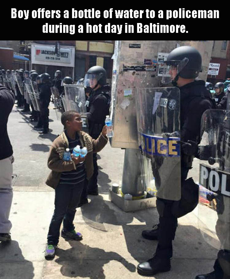 kids vs police - Boy offers a bottle of water to a policeman during a hot day in Baltimore.