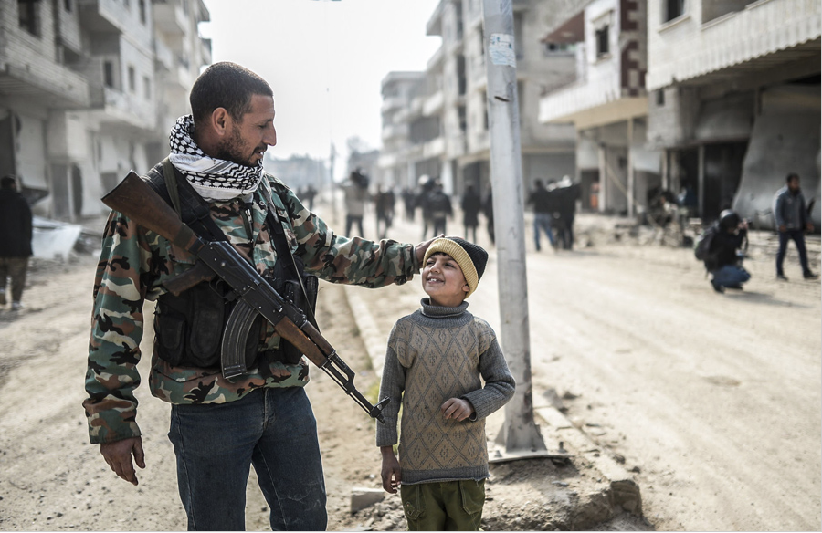 A Kurdish fighter walks with his child in the streets of Kobani, Syria after they recaptured it from ISIS militants