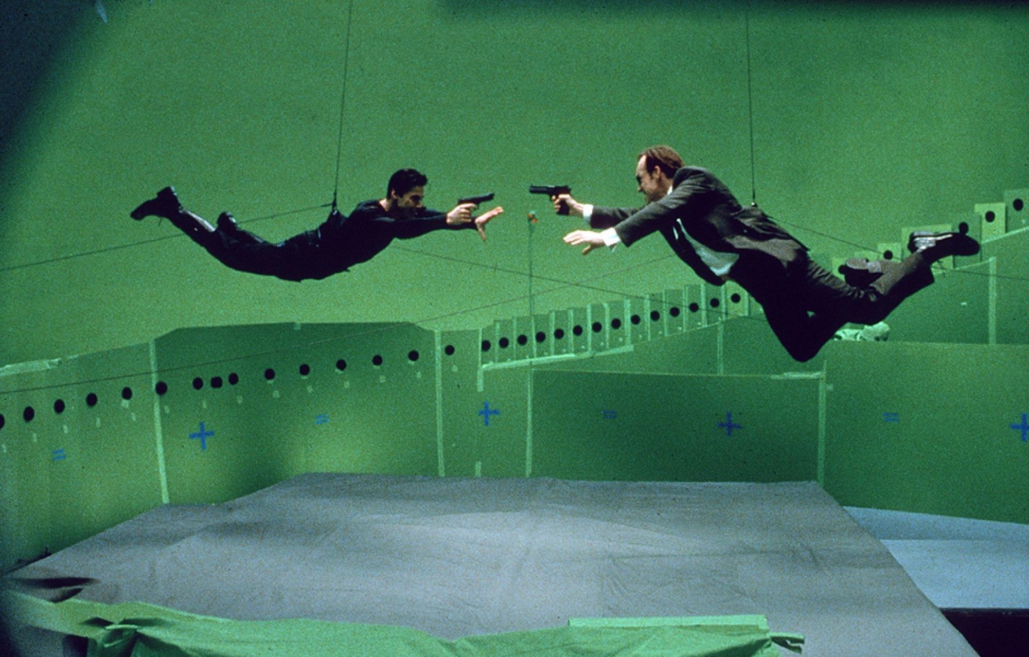 Keanu Reeves and Hugo Weaving shooting at each other in The Matrix.