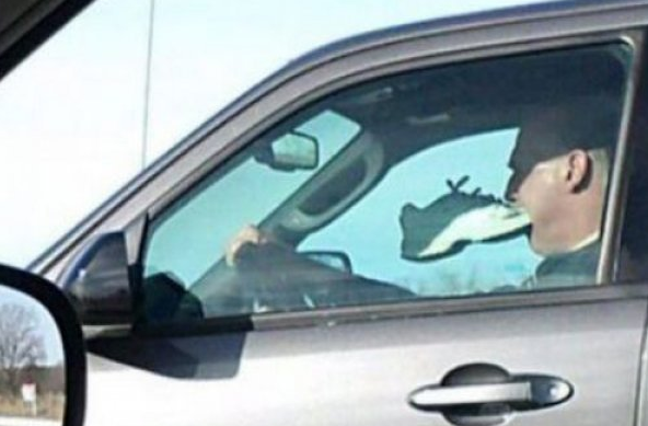 bizarre guy driving with shoe in mouth
