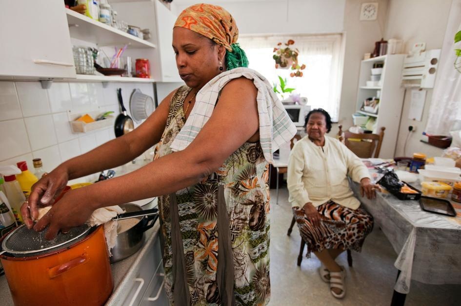 A woman prepares a Surinamese cake as her grandmother watches at a retirement home in Amsterdam.