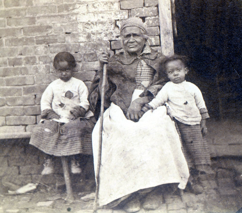 1867: Betty Jackson, was one of over 300 slaves owned by U.S. President Andrew Jackson throughout his lifetime. She is pictured in front of a slave cabin with two little girls.