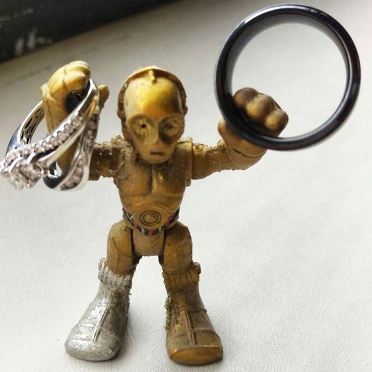 A mini C-3PO holding all the wedding bands found on the beach