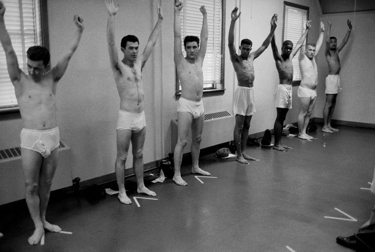 U.S. Army Pvt. Elvis Presley (3rd from left) raises his arms along with several other inductees at Fort Chaffee, Ark, 1958