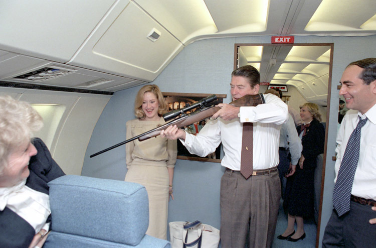 President Ronald Reagan aiming a rifle at a window aboard Air Force One in 1983.