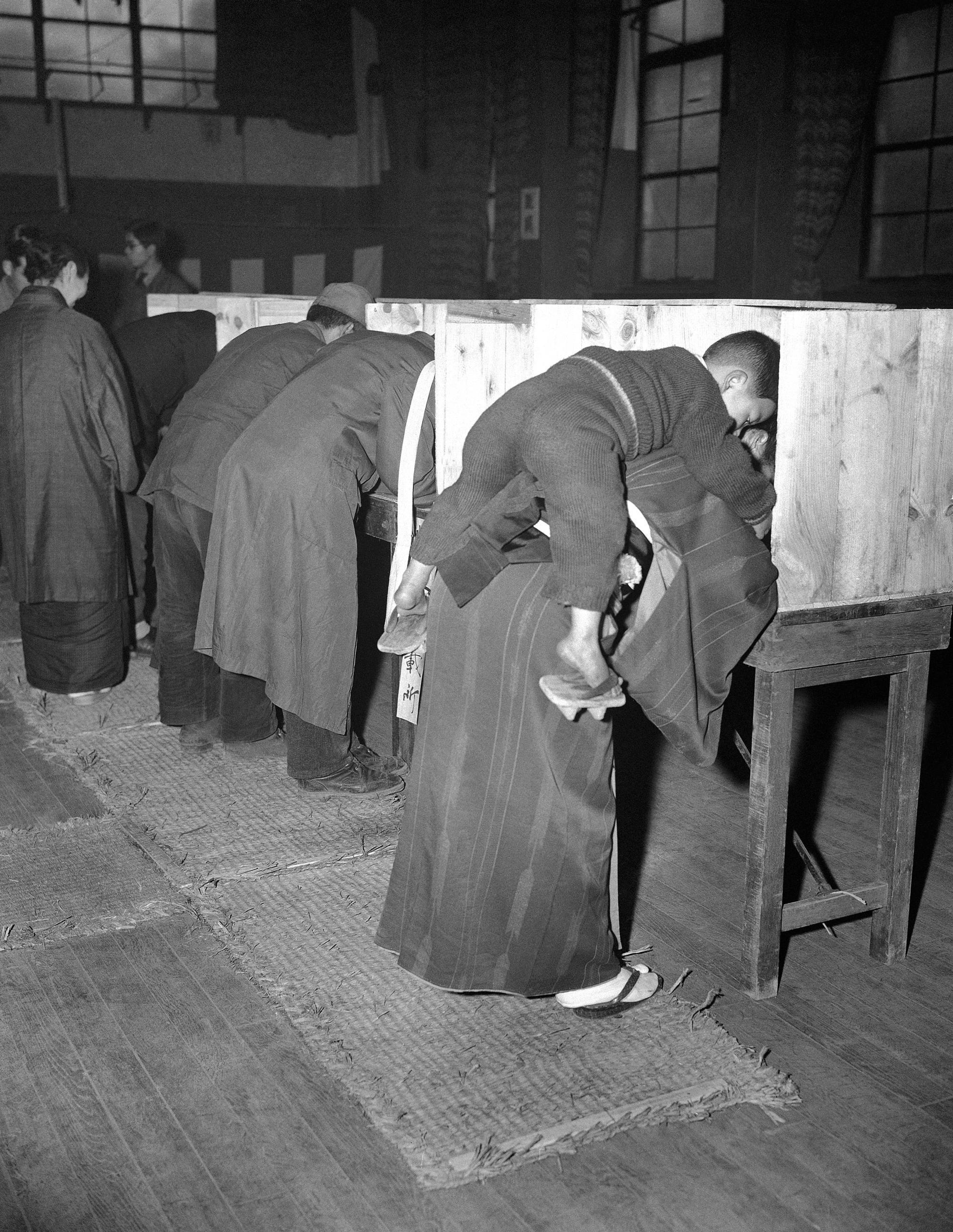 A Japanese woman carries her son on her back as she marks her ballot. This was in the first free election in 1946 Tokyo.