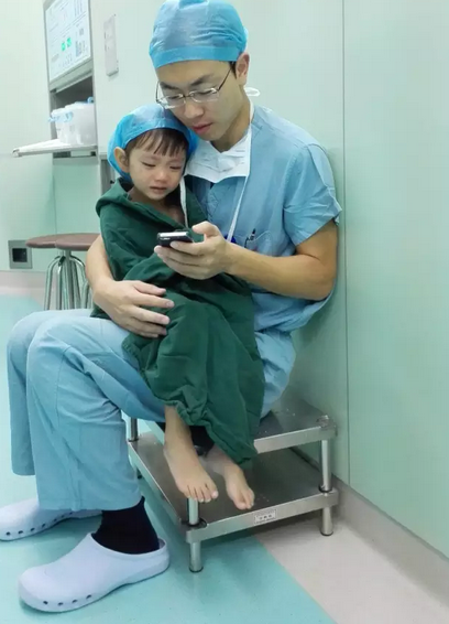 Cardiac surgeon comforts a weeping 2-year-old girl by playing cartoons before her surgery