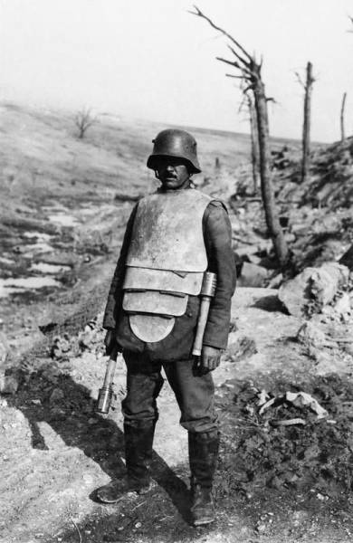 WWI: A German member of a “Trench Attack Squad” poses in steel body armor and two stick grenades.