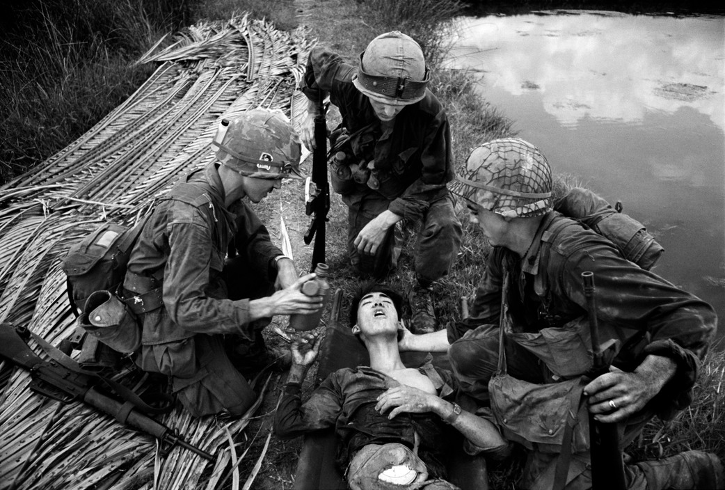 American soldier offers water to a wounded VC. He had been fighting for three days with his entrails been held in place only by a cooking pot tied to his belly. (1968, Vietnam)