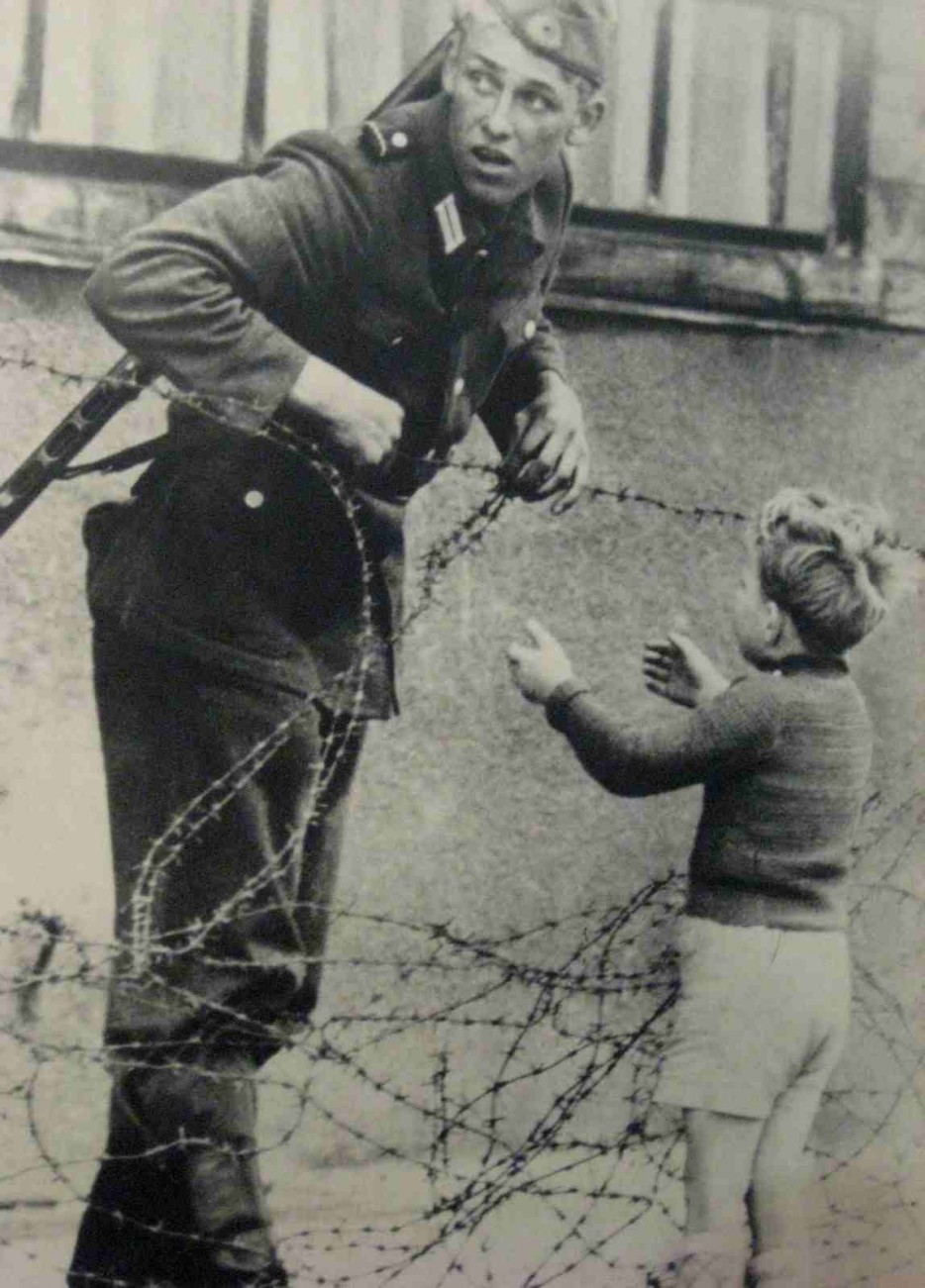 An East German soldier ignores orders to let no one pass and helps a boy, who was found on the opposite side from his family, cross the newly formed 'Berlin Wall'. [Cold War, 1961]