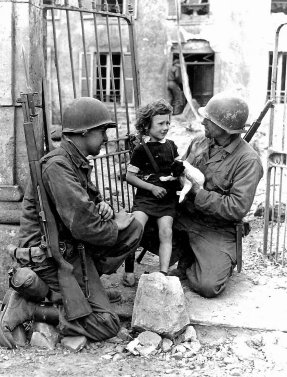 Two American soldiers try to comfort an upset girl with a puppy. [World War II, 1944]