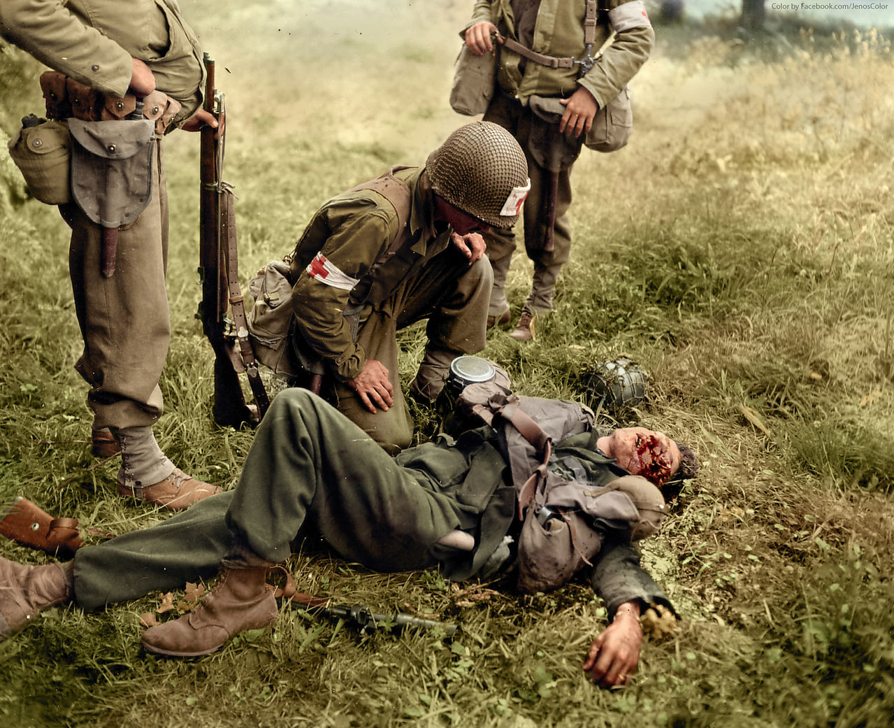 An American medic tends to a seriously injured German soldier who appears unconscious or dead, Normandy, Saint-Lo, June 1944.