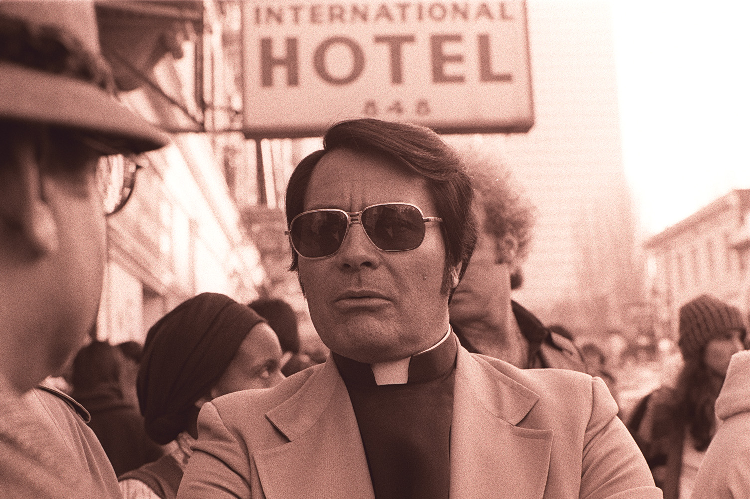 Monochrome photograph of cult leader Jim Jones wearing sports jacket and priests collar