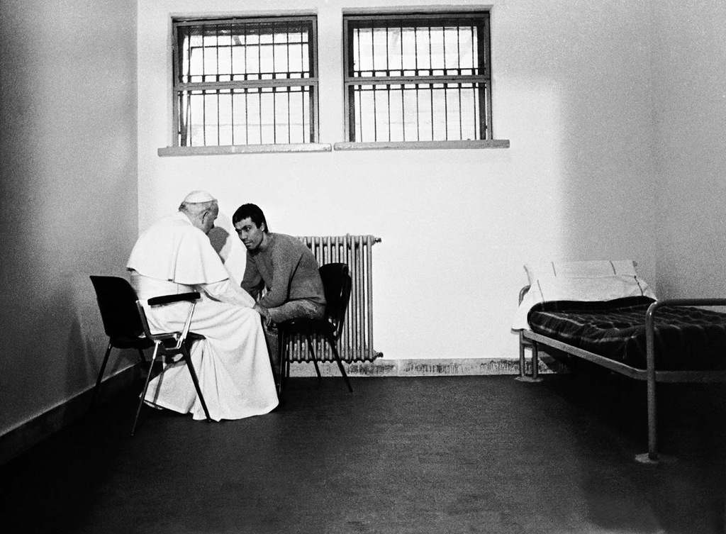 Pope John Paul II meets with Mehmet Agca, the man who attempted to assassinate him, 1983.
On Wednesday, May 13, 1981, Mehmet Ali Agca pulled a gun and shot Pope John Paul II during a procession in St. Peter’s Square, Vatican City, Italy. Though critically wounded, the Pope survived four gunshot wounds to his abdomen. Following the shooting, Pope John Paul II asked people to “pray for my brother…whom I have sincerely forgiven”.
In 1983, Pope John Paul II and Agca met and spoke privately at the prison where Agca was being held. The Pope brought the photographer and the cameramen because he wanted the image in that cell to be shown around a world filled witt unforgiving hatreds, with hostile superpowers and smaller, implacable fanaticism. When the Pope arrived in his cell, Agca was dressed in a blue crewneck sweater, jeans and blue-and-white running shoes from which the laces had been removed. He was unshaved. Agca kissed John Paul’s hand. “Do you speak Italian?” the Pope asked. Agca nodded. For 21 minutes, the two men seated themselves, close together, on molded-plastic chairs in a corner of the cell, out of earshot.
As John Paul rose to leave, the two men shook hands. The Pope gave Agca a small gift in a white box, a rosary in silver and mother-of-pearl. The Pope walked out. Agca was left standing alone, and the camera recorded a sudden look of uncertainty on his face. Perhaps he was thinking about the prospect of spending the rest of his life in jail for attempting to kill a man he did not know, a man who now came to him as a friend.
Agca was sentenced, in July 1981, to life imprisonment in Italy for the assassination attempt, but was pardoned by president Carlo Azeglio Ciampi in June 2000 at the Pope’s request. He was then extradited to Turkey, where he was imprisoned for the 1979 murder of left-wing journalist Abdi İpekçi and two bank raids carried out in the 1970s. Despite a plea for early release in November 2004, a Turkish court announced that he would not be eligible for release until 2010.
Nonetheless he was released on parole on 12 January 2006. However, on 20 January 2006, the Turkish Supreme Court ruled that his time served in Italy could not be deducted from his Turkish sentence and he was returned to jail. Ağca was released from prison on 18 January 2010, after almost 29 years behind bars.