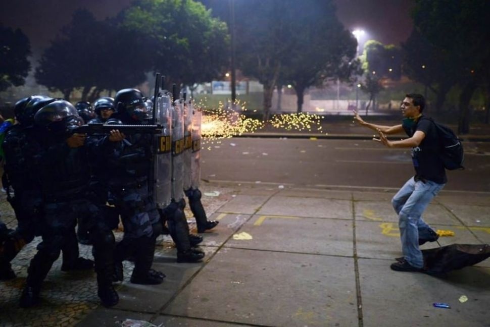 A Brazilian protester standing before gunfire during protests against police brutality and corruption.