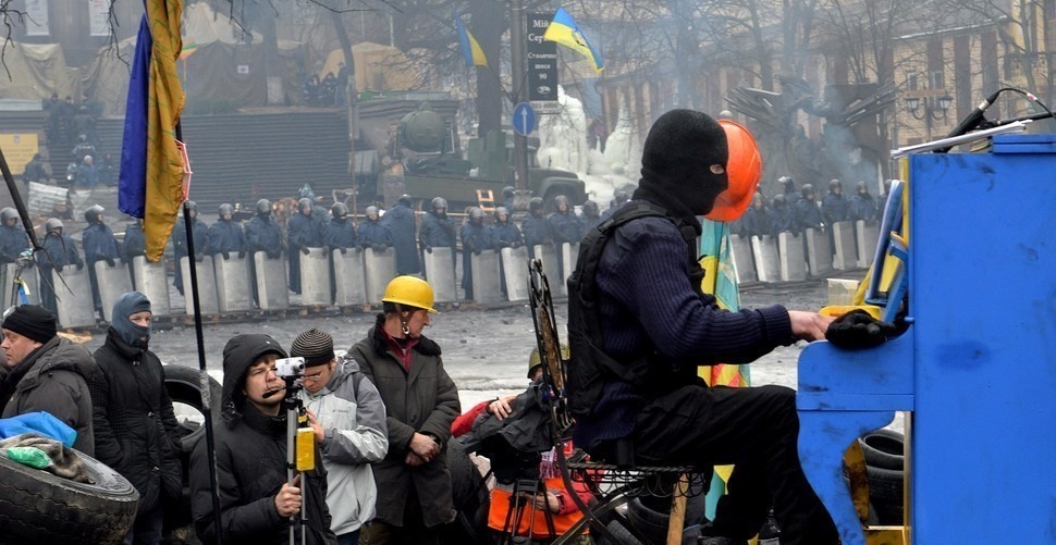 Protesters calmly playing piano over the loud sounds of chaos in the midst of a riot.