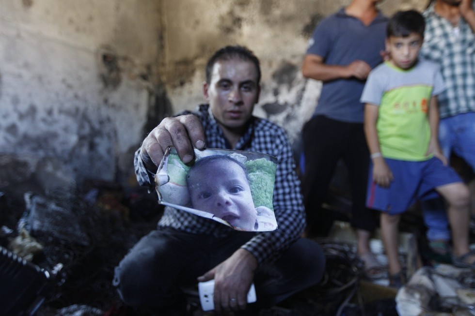 A man holding a photo of a 18-month-old Ali Dawasbsheh after he was killed when suspected Jewish extremists threw firebombs into his family's home.