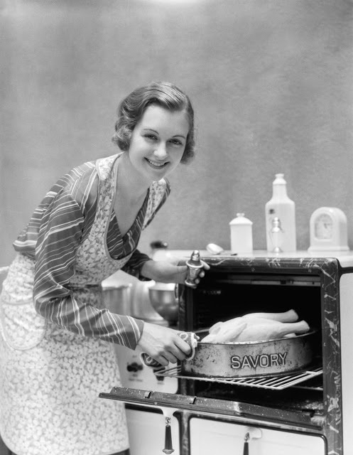 During the 1930's this housewife pulls a turkey from the oven as she smiles for the camera. The photo looks to be taken from an old commercial.
