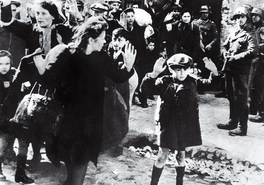 Jewish Boy Surrenders in Warsaw, 1943.
A 7-year-old boy raises his hands while standing alongside other Warsaw ghetto Jews as a German troop looks on. The scene captures the horror of the Holocaust. He says that his family was moved to a camp in western Germany. They moved to Israel at the end of the war but later migrated to the U.S.