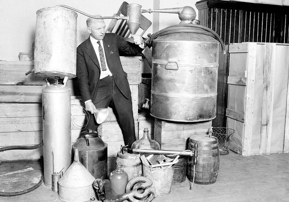 Edwin C. Arthur stands in the center of a collection of containers of moonshine taken during a South Side raid in Chicago, Illinois, 1922. From the Chicago Daily News collection