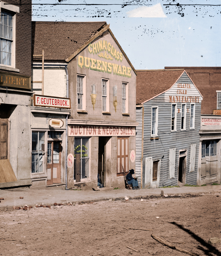 A black soldier of the Union army sits in front of a storefront with the text ‘Auction & Negro Sales’, ca. 1865, Atlanta, Ga.