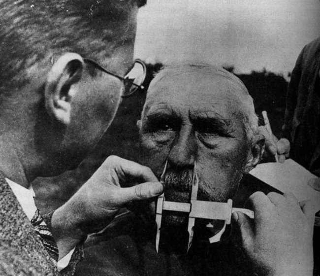 A man is having his nose measured by the Nazi police police to decide whether or not he is Jew. Hitler had a stereotype that Jewish noses are larger than Aryan noses.