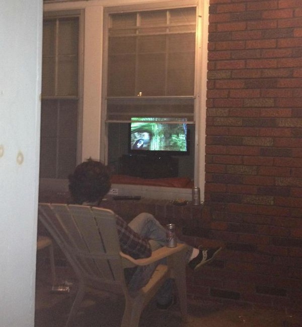 Dude watching TV outside while TV is inside.