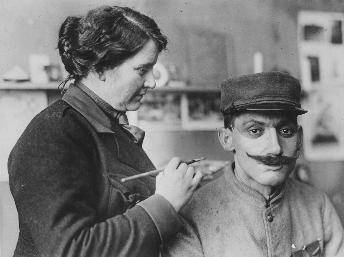 Masks made for men with disfigured faces from war wounds. Original caption: Mrs. Ladd coloring one of the masks after adjusting on a wounded Poilu’s face, 1917