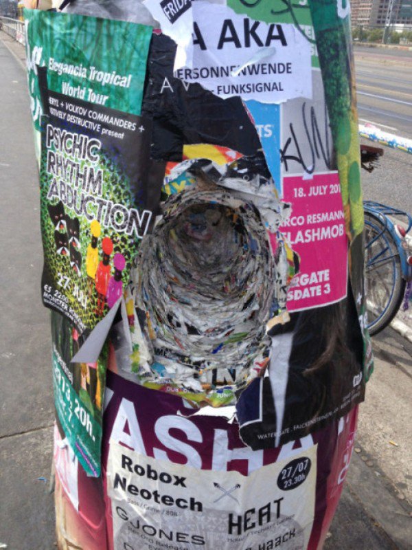 Layers of posters and flyers that have been affixed to the pole drilled right through.
