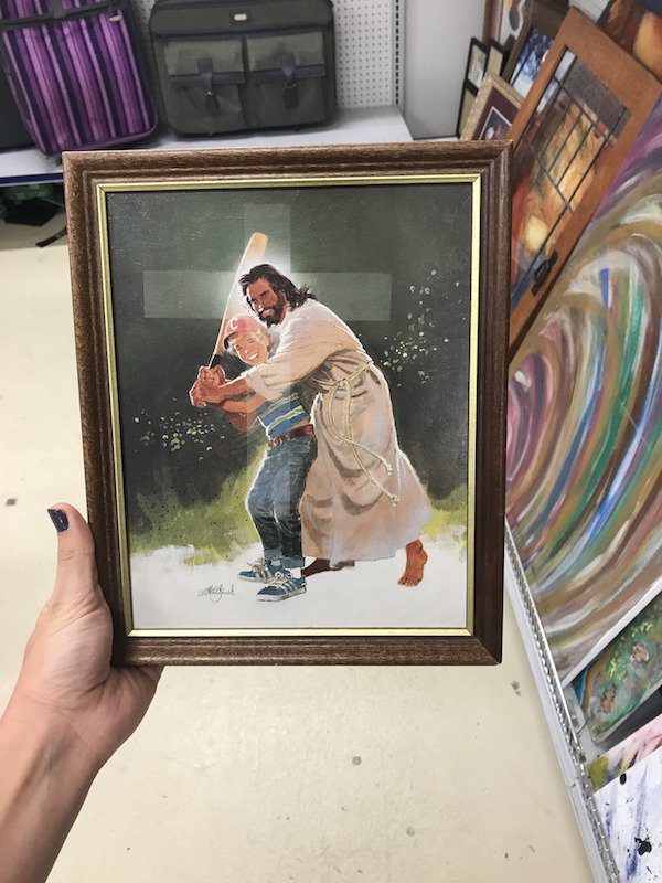 Jesus helping someone swing a bat in a framed photo in a thrift shop