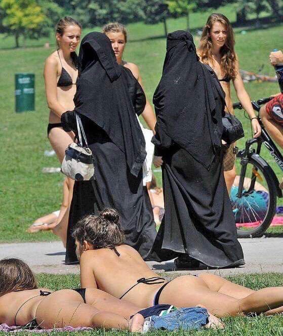 Women in burkas walking by women in bikinis