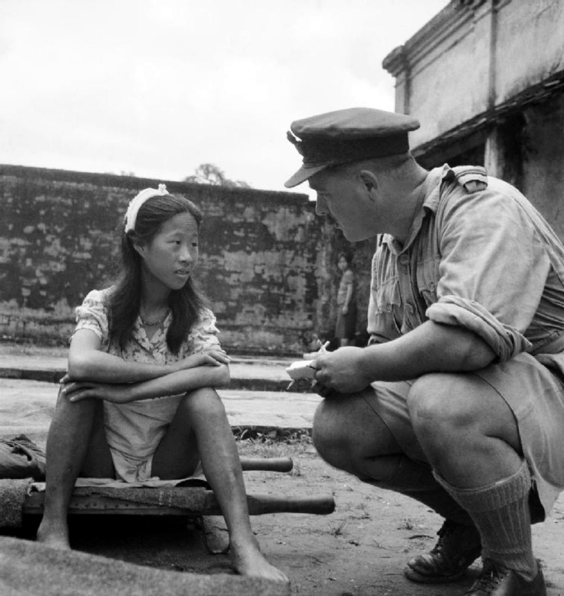 A young Chinese woman sits on a stretcher at a liberated “comfort station” as she is interviewed by a British Flying Officer of the Royal Air Force following the Allied victory in the Battle of Burma. 8 August 1945