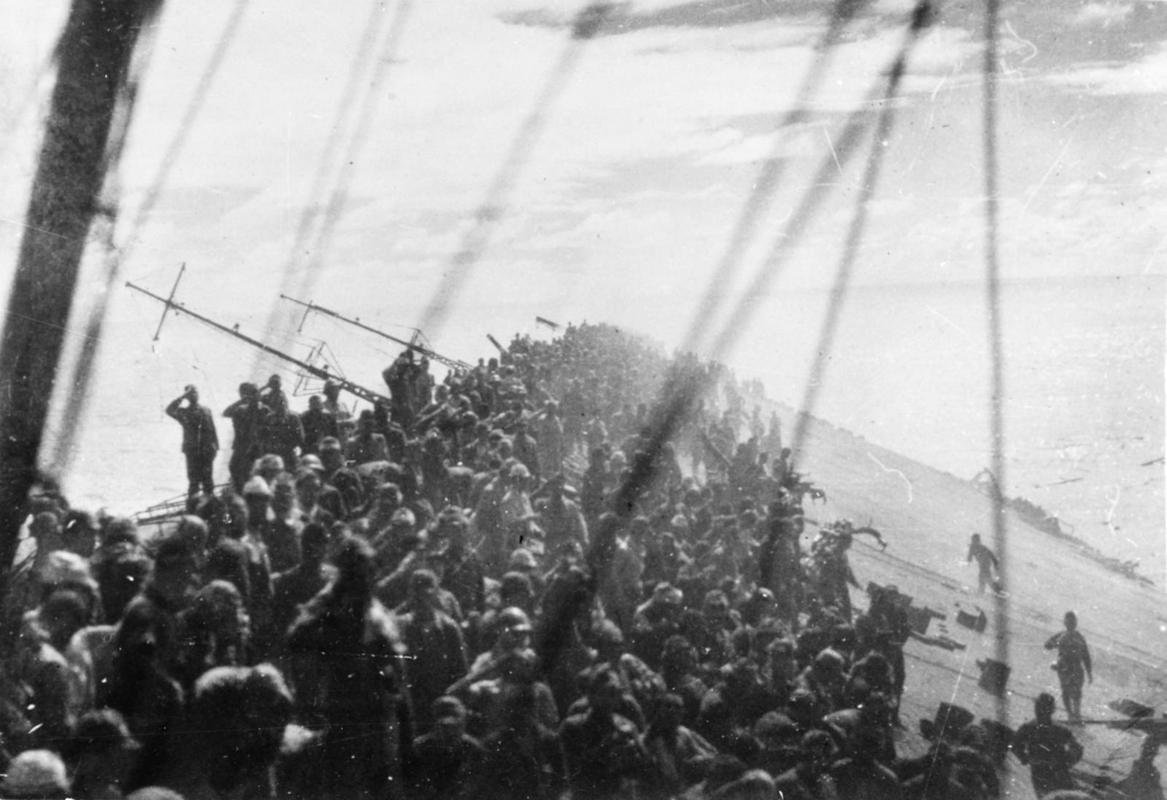The crew of the sinking Japanese air craft Zuikaku salutes as the flag is lowered for the last time on October 25, 1944. The ship would sink with the loss of 843 men