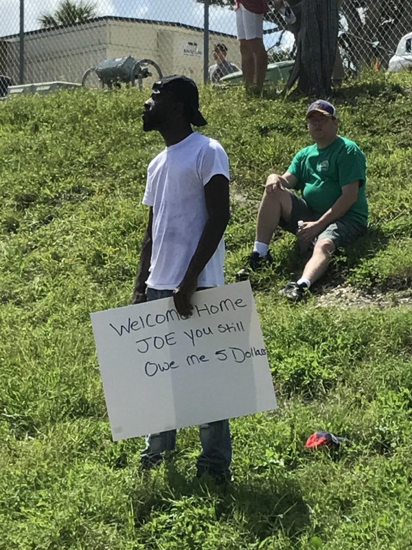 Man holding welcome sign for someone and pointing out he still owes him $5