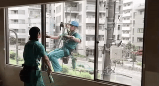 GIF of window cleaners working in total sync on opposite sides of the glass