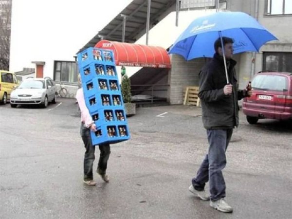 Man walking with umbrella and sipping a beer as the girl walks behind him carrying the cases of beer.