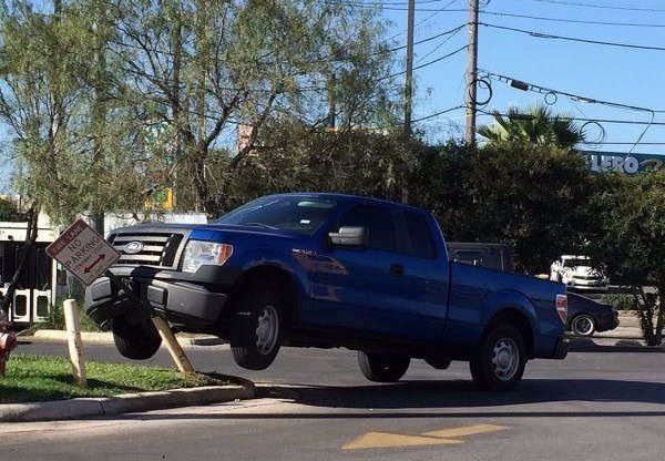 blue pickup truck stuck in the air on a pole