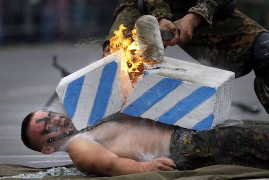 Man getting cinder block broken atop his chest by flaming sledgehammer.