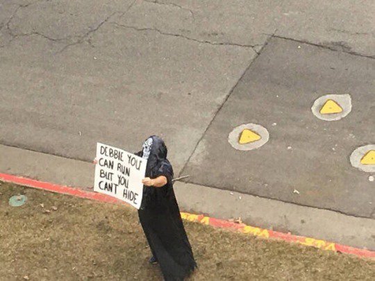 Man dressed as smiling ghost with sign referencing the movie SCREAM