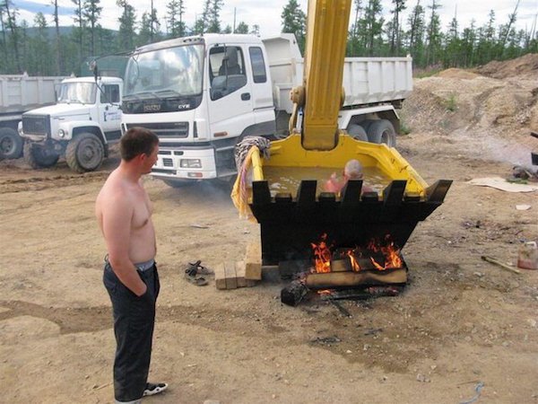 Man enjoying a hut tub in the cuff of an excavator over a wooden fire somewhere in Russia